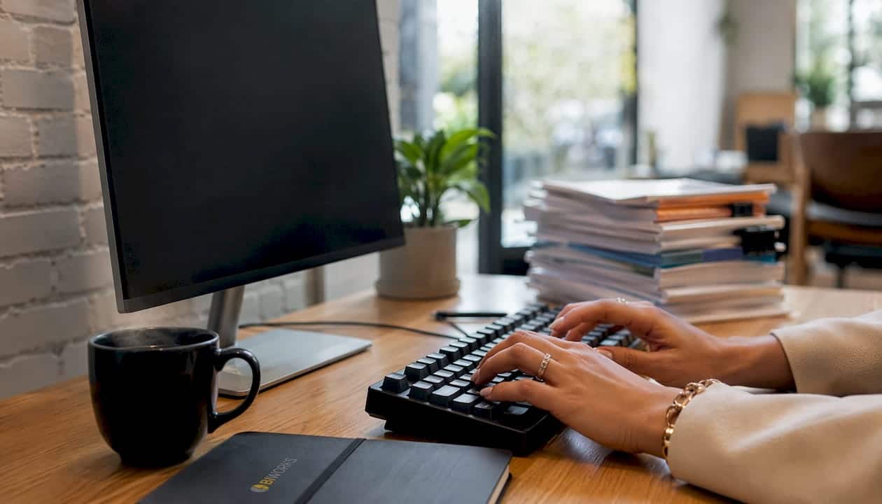 Poste de travail avec un ordinateur, des mains en train de taper sur le clavier, vue côté branchements et connectiques.