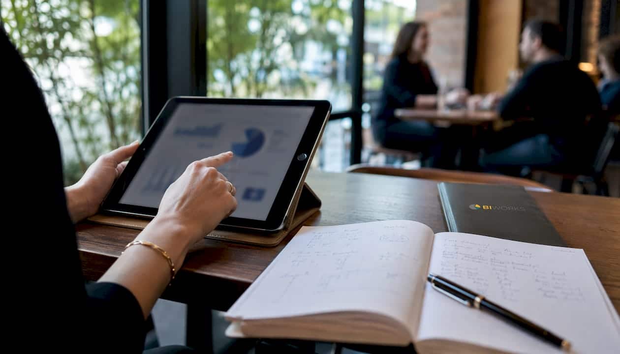 Un bureau sur lequel sont posés une tablette et un carnet, avec des mains qui manipulent les objets.